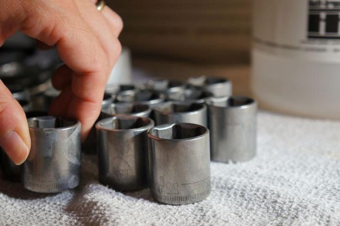 A photo of a socket set on a towel next to a hubbard hall cleaning solution. A hand is picking up one of the sockets.